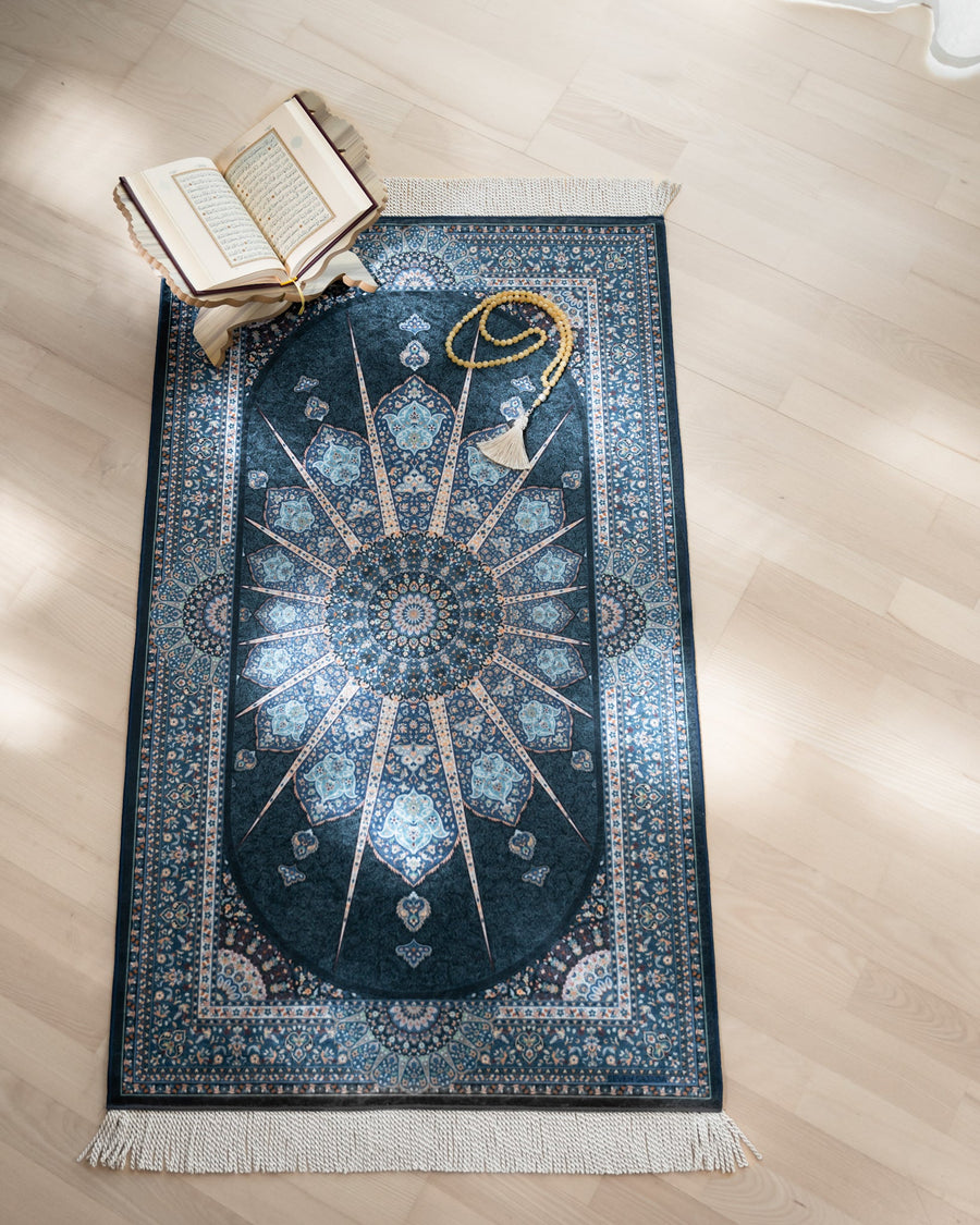 Blue Eye prayer mat on a light oak floor with an open Quran on a stand and an amber tasbih