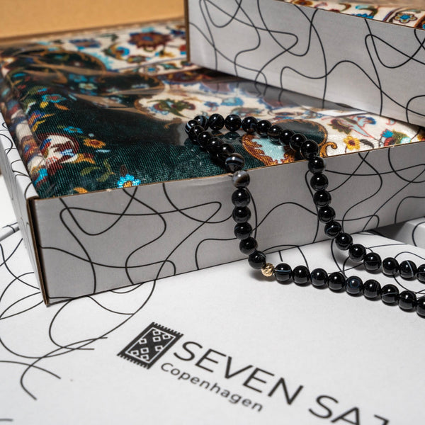 Black agate tasbih on an open Seven Sajada gift box holding a folded green prayer mat