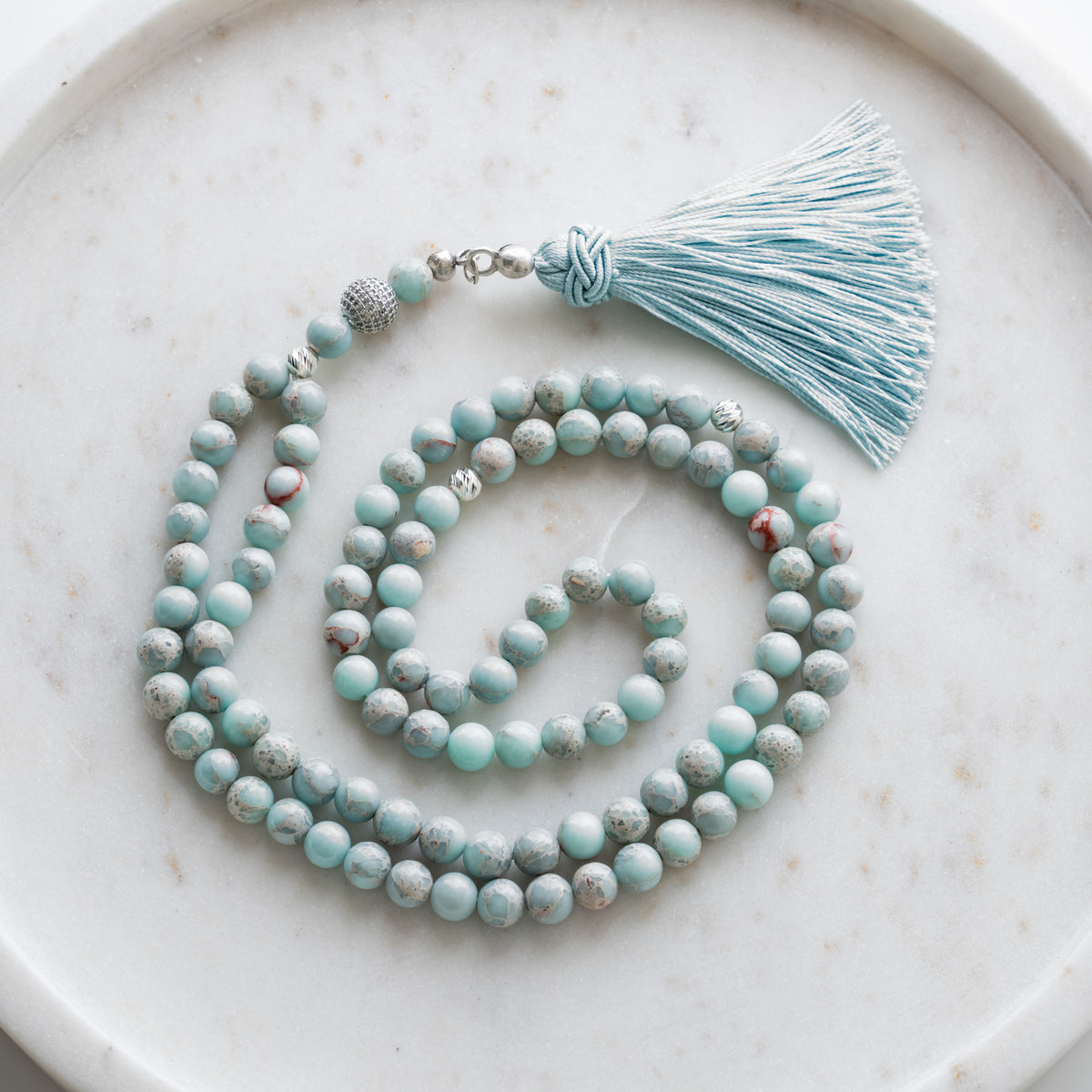 Tasbih (Misbaha) aus Varasit mit 99 Natursteinperlen, silbernen Zwischenperlen und hellblauer Quaste auf weißem Marmor